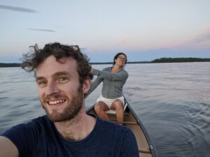 A man and woman in a canoe on the water, smiling at the camera