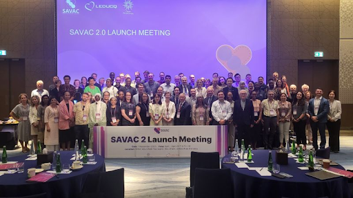 Group of approximately 50 people posing for a photo near a sign that says "SAVAC 2 Launch Meeting"